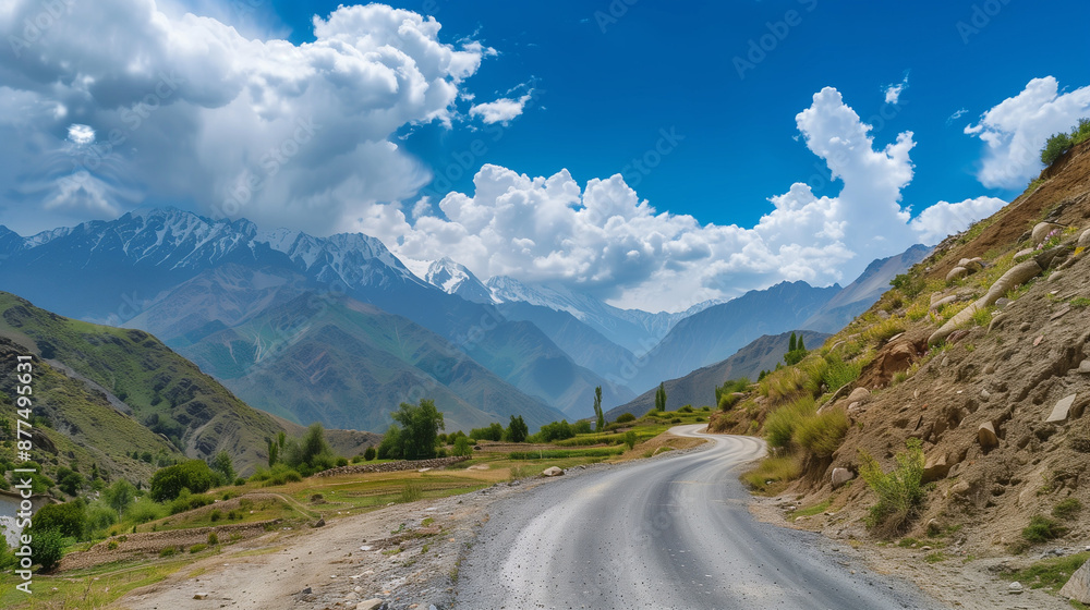 Fototapeta premium A picturesque road winding through the mountains under a clear sky with fluffy clouds in the background. This view exudes peace and beauty of nature, inviting you to travel through the landscape.