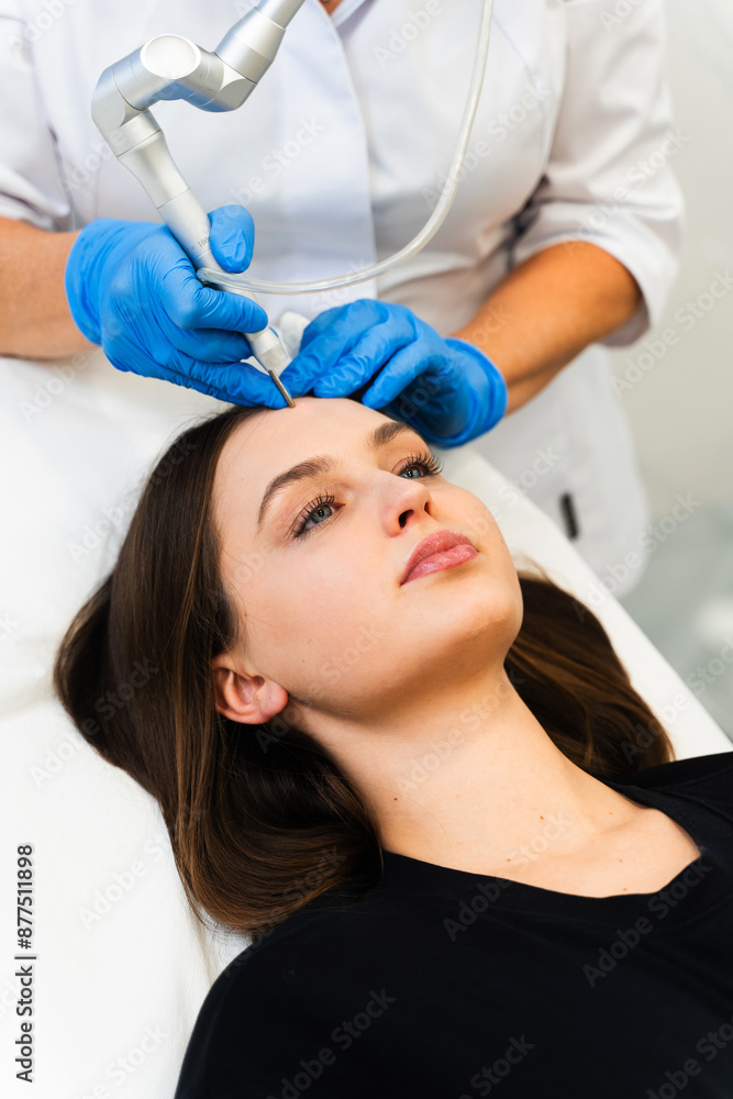 Laser removing moles and birthmarks from face of attractive girl. Cosmetologist applies laser device to cleanse skin of her patient.
