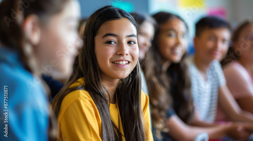 A cheerful young girl in a yellow shirt smiles brightly amid a group of diverse classmates in a lively classroom setting.
