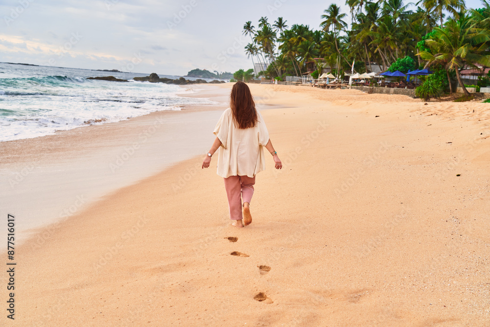 Back of calm solitude blissful boho woman walking along the sandy beach near the ocean at sunset time and enjoying beautiful moment life Back of calm solitude blissful boho woman walking along the sandy beach near the ocean at sunset time and enjoying beautiful moment life