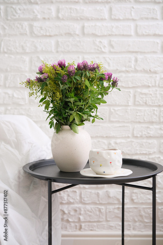 Light cozy bedroom, green tea cup and bouquet of flowers in ceramic vaze on black coffee table. photo