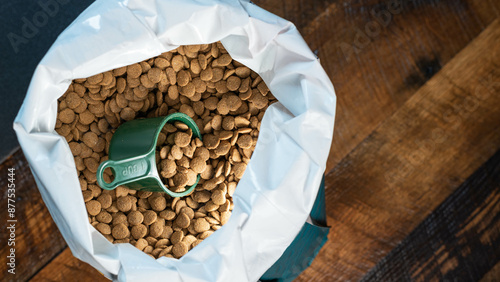 Green measuring cup full of dog or cat food kibble being removed from a bag in background.