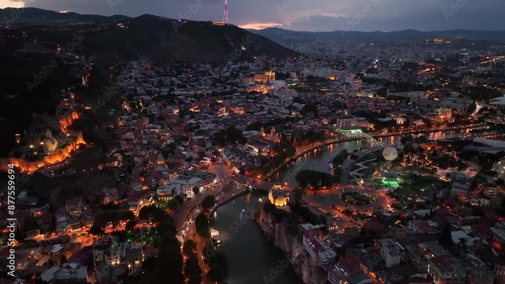 Tbilisi, Georgia. Scenic aerial view at twilight Of Famous Landmarks In Night Illuminations. Cityscape. Overview of the Kura (Mtkvari) River in Old Town, Tbilisi city central park and Bridge of Peace Tbilisi, Georgia. Scenic aerial view at twilight Of Famous Landmarks In Night Illuminations. Cityscape. Overview of the Kura (Mtkvari) River in Old Town, Tbilisi city central park and Bridge of Peace