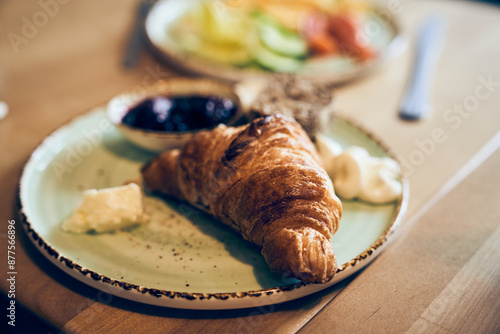 A view of the breakfast one croissant with jam on the background of a defocused plate with salad. With space to copy. High quality photo