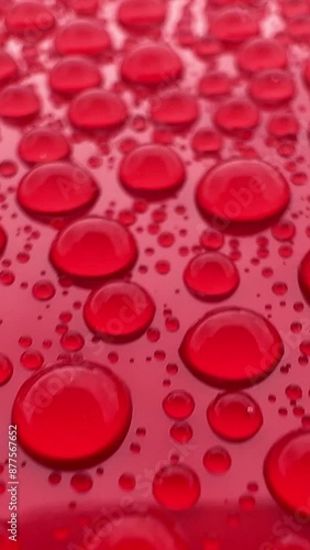 High-resolution footage showing hydrophobic effect with perfectly round water droplets on the surface of red car paint. Highlights the protective coating's quality and its ability to repel water.