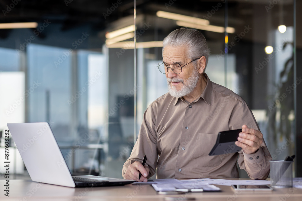 Senior businessman working on a laptop and holding a tablet in a modern office setting. The professional atmosphere showcases productivity, experience, and the use of technology business operations. Senior businessman working on a laptop and holding a tablet in a modern office setting. The professional atmosphere showcases productivity, experience, and the use of technology business operations.