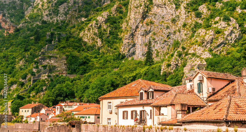 Fototapeta premium landscape of beautiful vintage houses with orange tile roofs in vintage venetian style to amazing high green mountain with ancient buildings on slopes and nice cloudy sky on background