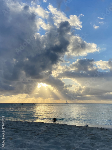 sunset over the sea with light beaming through the clouds. a little sail boat sits on the water  photo