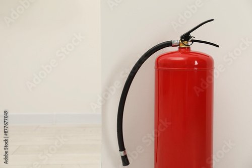 Fire extinguisher near light wall indoors, space for text