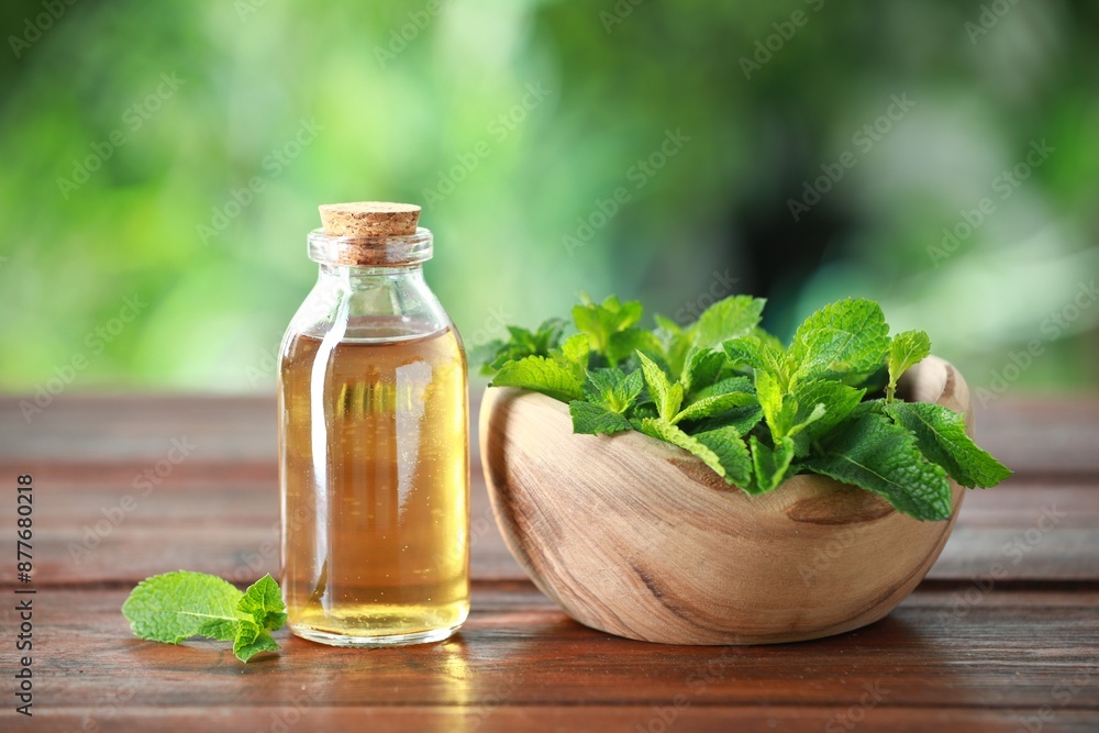 Bottle of mint essential oil and fresh leaves on wooden table Bottle of mint essential oil and fresh leaves on wooden table