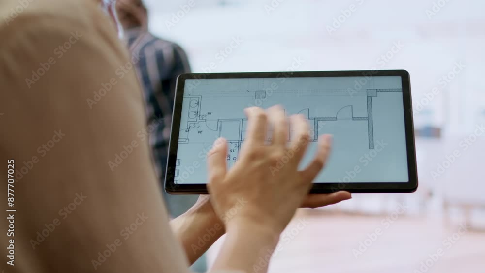 Real estate agent and client evaluating blueprints and discussing the architectural layout of new office space during office tour. Businessman strategizing corporate office relocation deal. Camera A. Real estate agent and client evaluating blueprints and discussing the architectural layout of new office space during office tour. Businessman strategizing corporate office relocation deal. Camera A.