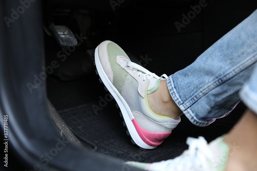 Woman in sneakers pushing on pedal of car brake, closeup