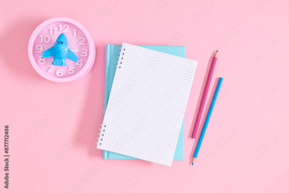Back to school concept. Flat lay top view of stack of notepads with empty space for text, stationery, alarm clock, sharpener in form of an airplane, pen and pencil isolated on pastel pink background. Back to school concept. Flat lay top view of stack of notepads with empty space for text, stationery, alarm clock, sharpener in form of an airplane, pen and pencil isolated on pastel pink background.