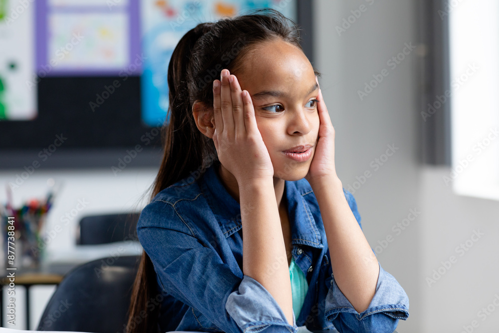 Stressed biracial schoolgirl sitting at desk in class, head in hands, looking away, copy space Stressed biracial schoolgirl sitting at desk in class, head in hands, looking away, copy space