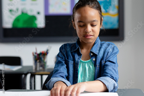 Blind biracial schoolgirl sitting at desk in class reading braille, with copy space