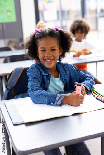Portrait of happy african american schoolgirl sitting at desk in school classroom