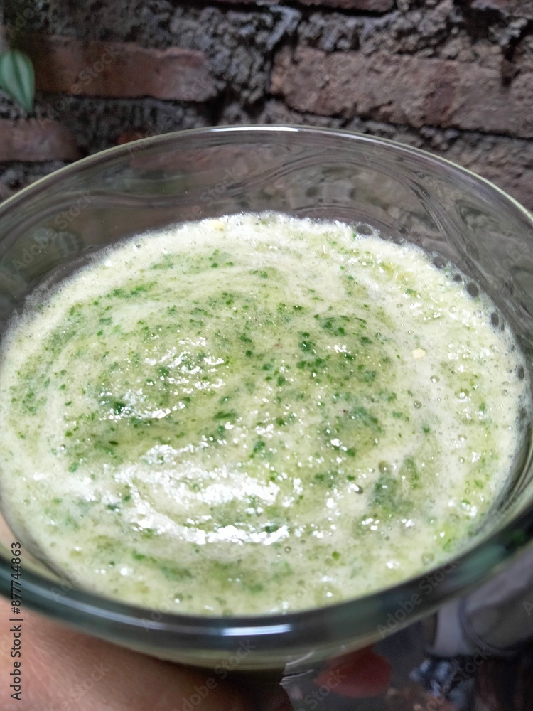 the hand holding a glass of smoothie that contain any vegetables with brick wall background. the hand holding a glass of smoothie that contain any vegetables with brick wall background.