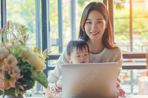 Asian Woman Professional Mom Multitasking with Baby Toddler Child on Lap while Working from Home with Flexible Schedule