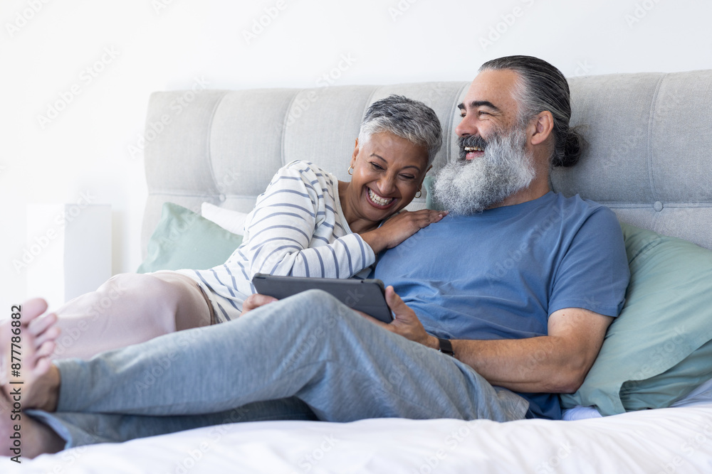 Relaxing on bed, senior couple smiling and using digital tablet together Relaxing on bed, senior couple smiling and using digital tablet together