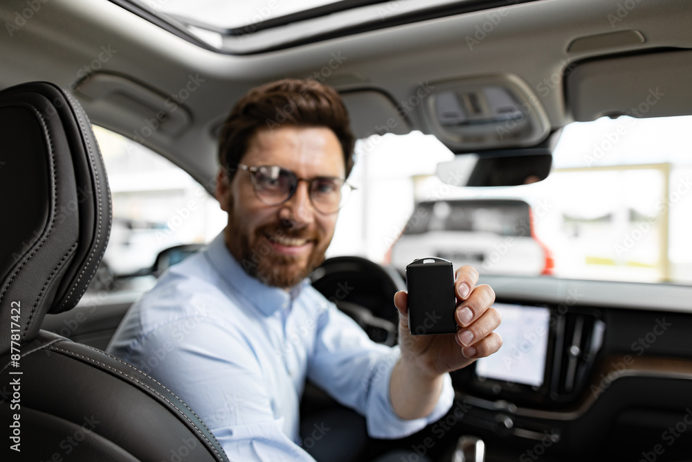 Concept of new car purchase, success, and business achievement. Smiling businessman sits inside car at dealership holding car key.Luxurious interior visible in this modern vehicle. Concept of new car purchase, success, and business achievement. Smiling businessman sits inside car at dealership holding car key.Luxurious interior visible in this modern vehicle.