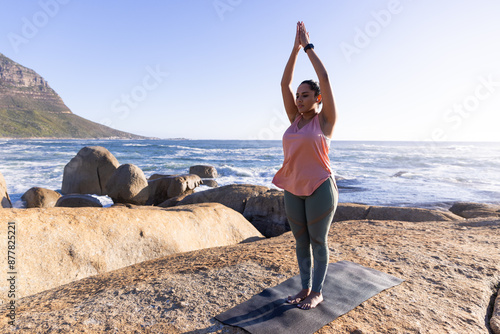 Practicing yoga on mat, mature woman doing mountain pose by ocean, copy space