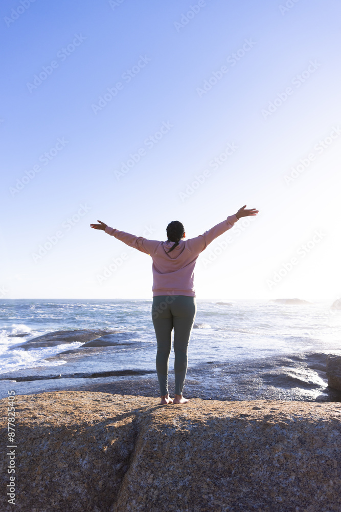 Standing on rocky shore, woman stretching arms and enjoying ocean view Standing on rocky shore, woman stretching arms and enjoying ocean view