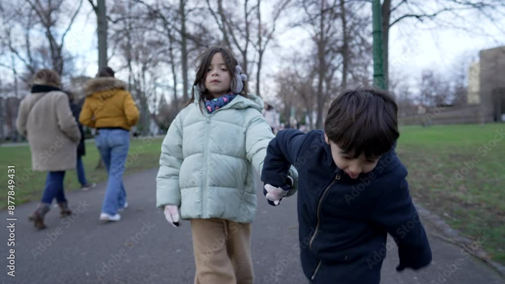 Childrens Holding Hands In Winter Coats Walking In Park During Cold Day In A Quiet Urban Landscape. Bonding Moments Between Siblings Childrens Holding Hands In Winter Coats Walking In Park During Cold Day In A Quiet Urban Landscape. Bonding Moments Between Siblings