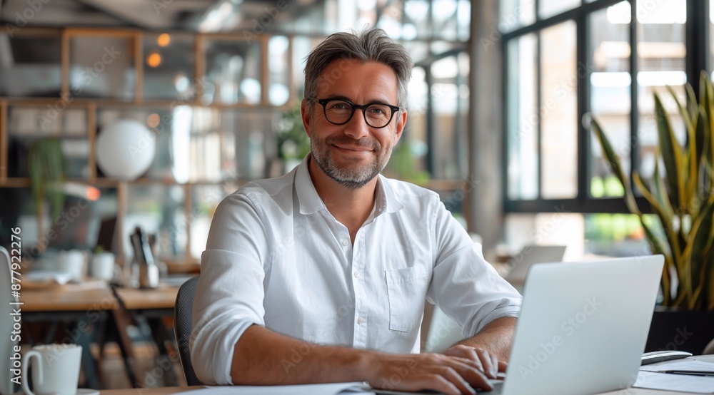 happy male accountant with income tax documents and laptop working at desk in a modern office with a glass-wall interior. happy male accountant with income tax documents and laptop working at desk in a modern office with a glass-wall interior.