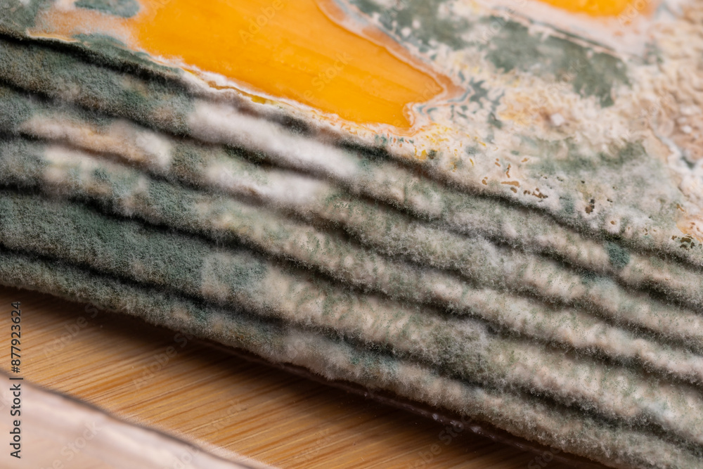 Slices of moldy yellow cheese arranged on a bamboo cutting board. Green mold spores on food. Expired wasted food