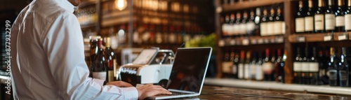 Man using laptop at wine shop counter, surrounded by bottles, digital point of sale system in use, modern retail technology in wine store.