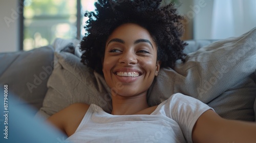 A smiling woman lying down on a couch with a pillow, perfect for representing relaxation and leisure