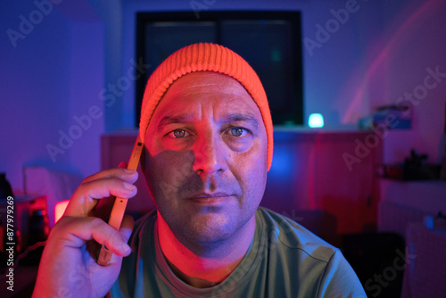 A gamer talking on his smartphone while playing an online video game. The man likes to spend his free time at home. Neon lights. photo