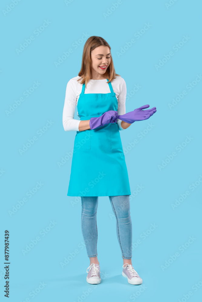 Young woman putting rubber gloves on blue background Young woman putting rubber gloves on blue background