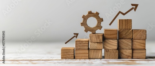 Wooden blocks stacked in an upward trend with a gear on top and arrows symbolizing growth.