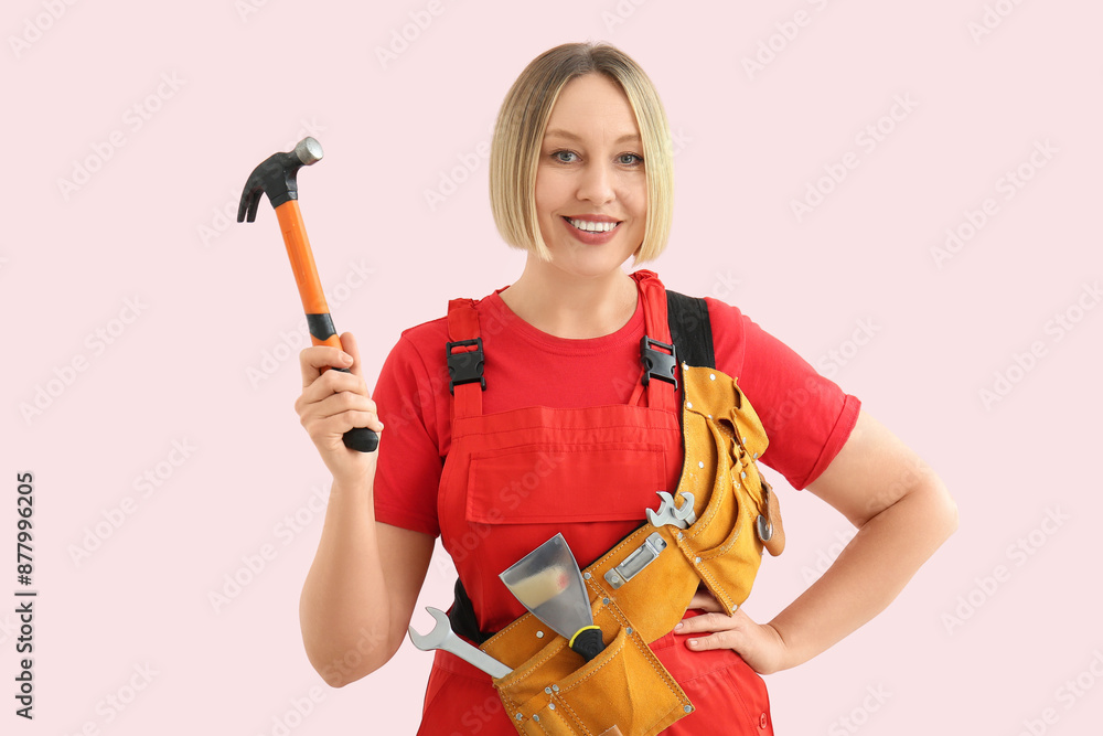 Female worker with tools belt and hammer on pink background Female worker with tools belt and hammer on pink background