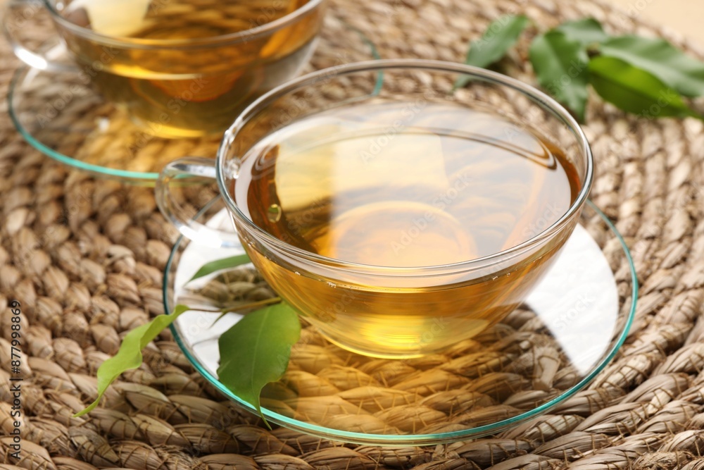 Refreshing green tea in cup and leaves on wicker mat, closeup Refreshing green tea in cup and leaves on wicker mat, closeup