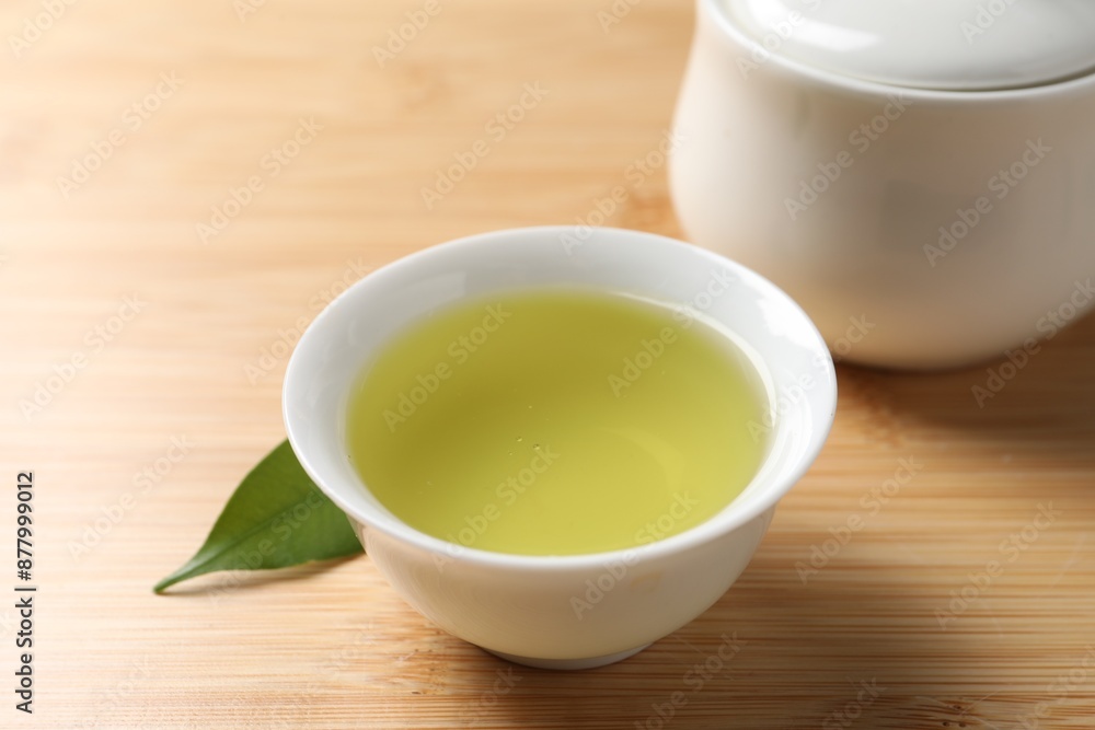 Refreshing green tea in cup, sugar bowl and leaf on wooden table, closeup Refreshing green tea in cup, sugar bowl and leaf on wooden table, closeup