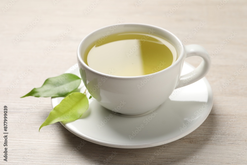 Refreshing green tea in cup and leaves on wooden table, closeup Refreshing green tea in cup and leaves on wooden table, closeup