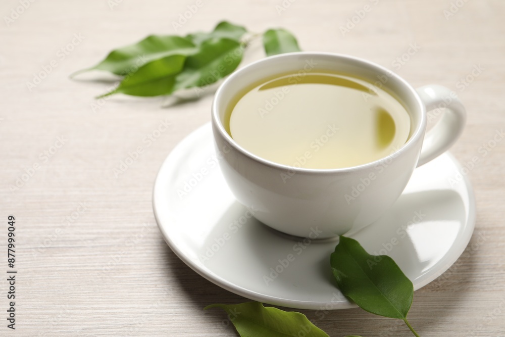 Refreshing green tea in cup and leaves on wooden table, closeup Refreshing green tea in cup and leaves on wooden table, closeup