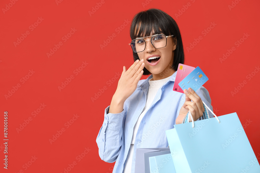 Surprised young woman with credit cards and shopping bags on red background Surprised young woman with credit cards and shopping bags on red background