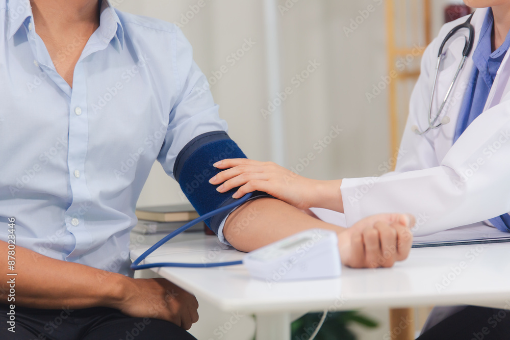Fototapeta premium Female doctor uses digital blood pressure monitor Measuring blood pressure of male patient in hospital. Concept of medicine and health care.