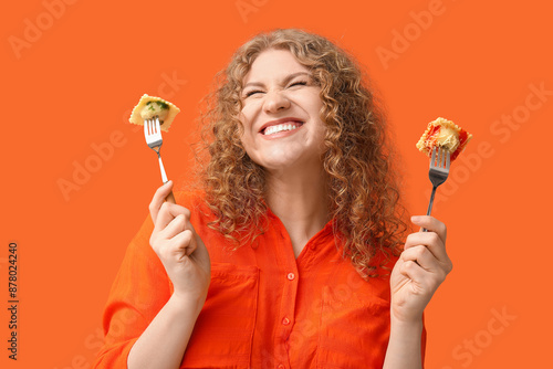 Fototapeta Happy young woman holding forks with tasty ravioli on orange background