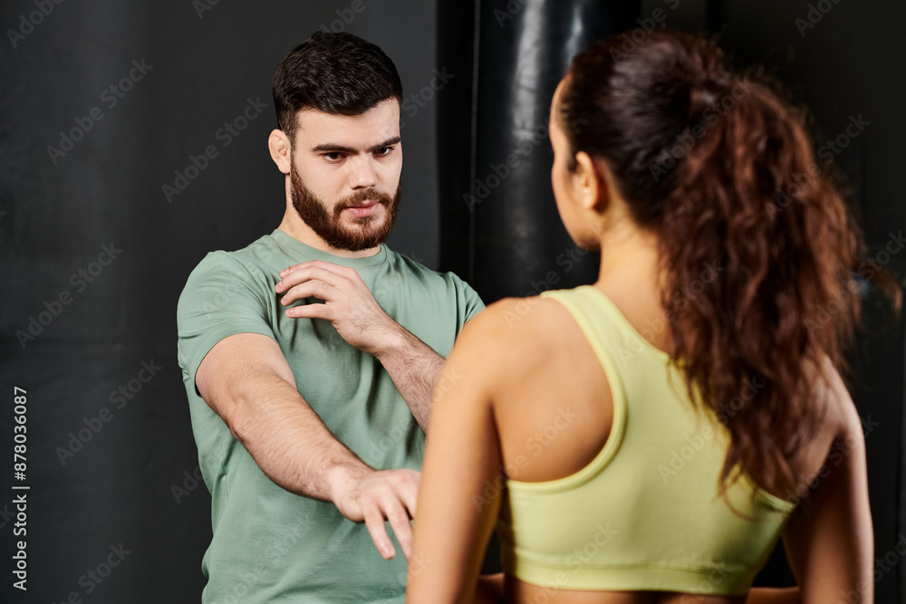 A male trainer demonstrates self-defense techniques to a woman in a gym. A male trainer demonstrates self-defense techniques to a woman in a gym.