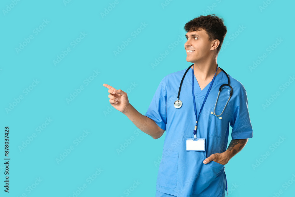 Male medical student with stethoscope and badge pointing at something on blue background Male medical student with stethoscope and badge pointing at something on blue background
