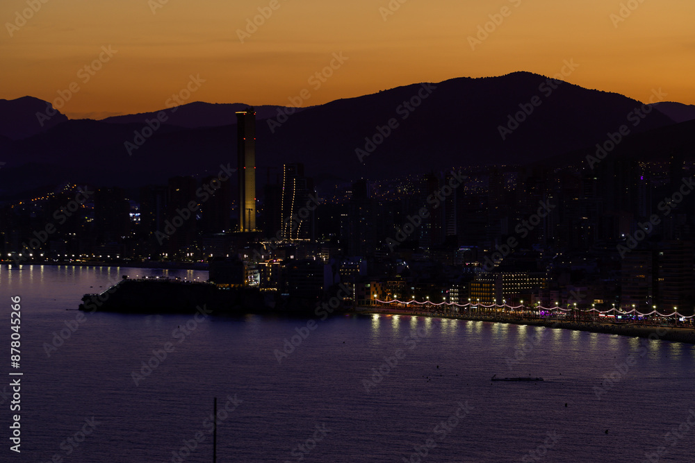 Fototapeta premium Night time aerial photo of Benidorm Playa Levante beach in the evening showing the sun setting behind the mountains and the hotels and high rise apartments on the beach front