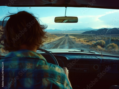 A focused driver is behind the wheel, with a view of the road and a beautiful landscape ahead, as seen through the windshield of the car on a sunny day.