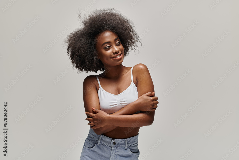 A stylish young African American woman proudly stands with her arms crossed, showcasing her stunning afro. A stylish young African American woman proudly stands with her arms crossed, showcasing her stunning afro.