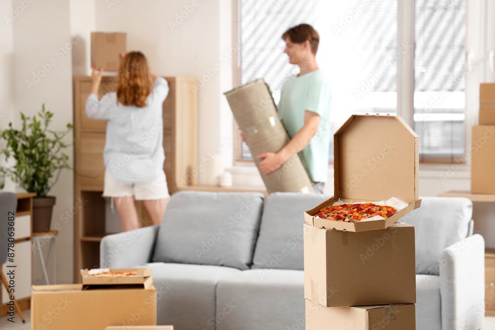 Beautiful young couple and cardboard box with tasty pizza in living room on moving day Beautiful young couple and cardboard box with tasty pizza in living room on moving day