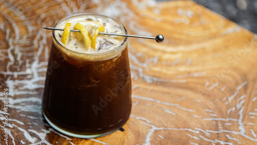 a glass of iced lemon coffee garnished with a fresh lemon slice on a wooden table with space to the right of the glass