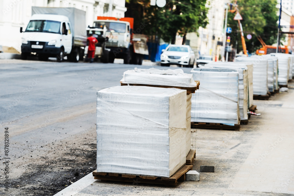 Obraz premium Paving stones in packages delivered by a building materials supplier. Construction and repair of pedestrian paths on a city street. Foreground. Selective Focus